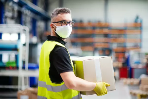 Man wearing face mask and uniform carrying a box inside a warehouse