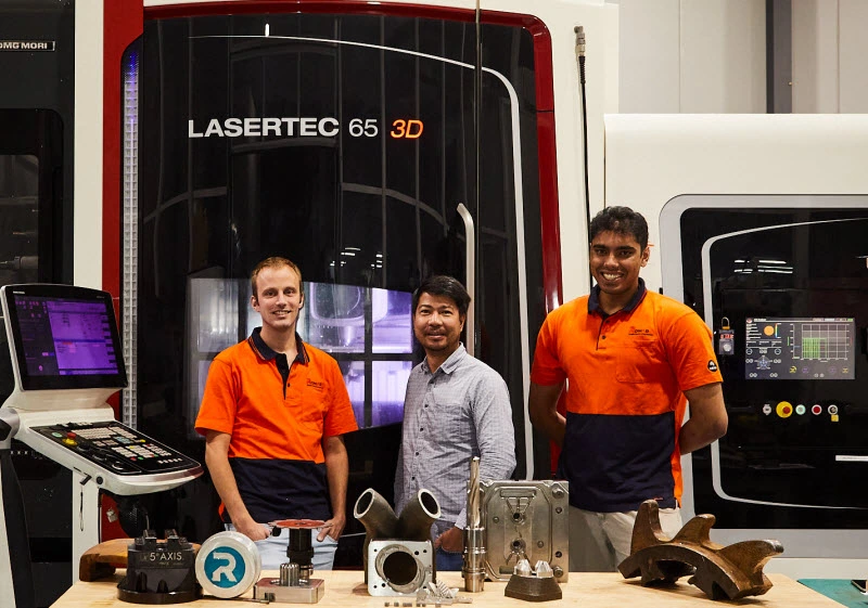 Three employees standing in front of Lasertec 3D machine with steel equipment on the table
